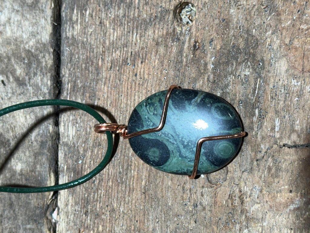 Green and black swirled stone on a green leather necklace.