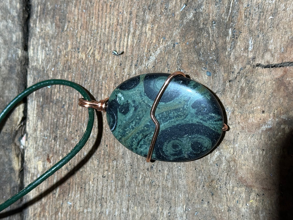 Green and black swirled stone on a green leather necklace.