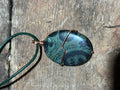 Green and black swirled stone on a green leather necklace.