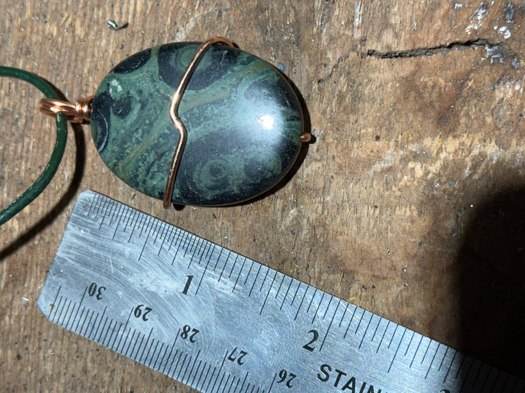 Green and black swirled stone on a green leather necklace.